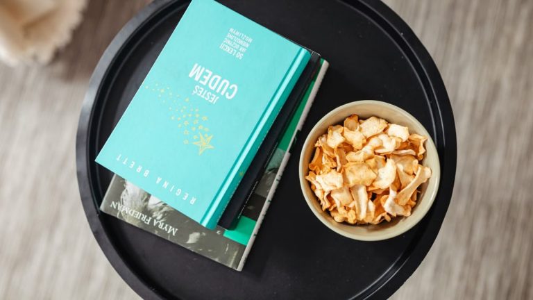 Aerial view of a stack of books and a snack bowl on a round table, creating a cozy reading nook.