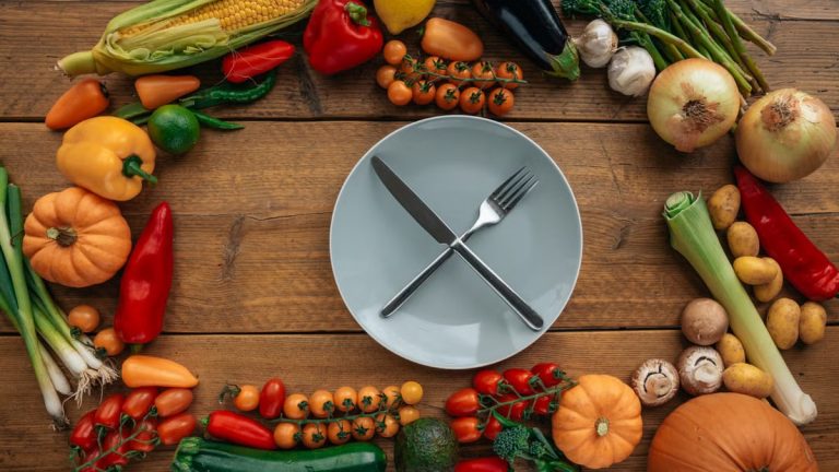 Top view of fresh vegetables creatively arranged around an empty plate on a wooden table.